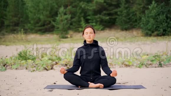女人坐在沙滩上做瑜伽时正在冥想视频的预览图