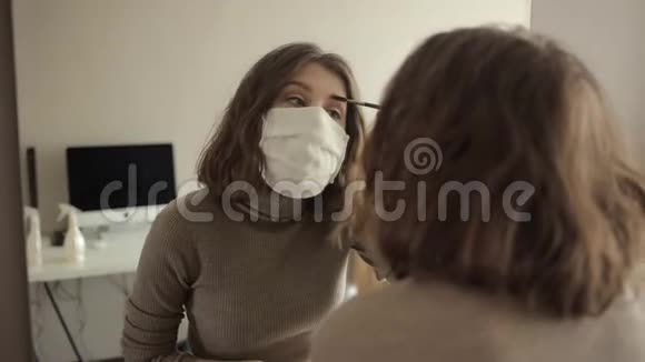 戴着防护面罩的年轻女孩在家中被隔离时在镜子前化妆冠状病毒COVID视频的预览图