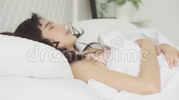 美丽的亚洲年轻女子躺在床上头靠在枕头上舒适而快乐地躺在卧室里视频的预览图