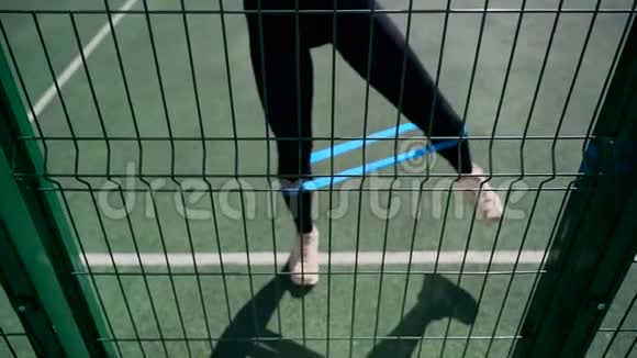 篮球场上的女孩做运动使用健身橡皮筋站立时将腿放在一边视频的预览图