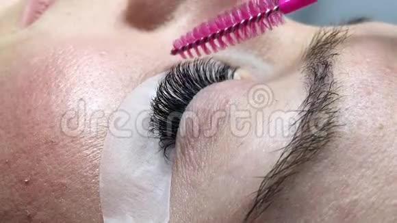 一个闭着眼睛躺着的女人的特写主人用一支粉红色的刷子梳着长长的睫毛视频的预览图