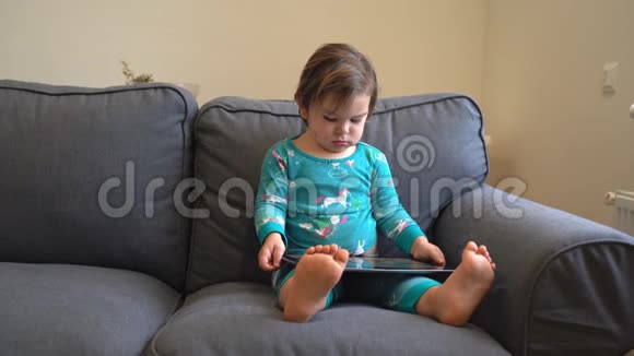 幼儿坐在沙发上在平板电脑上玩游戏看动画片现代童年视频的预览图