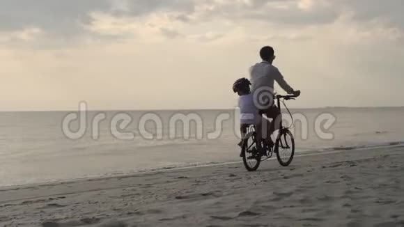 快乐的亚洲家庭父亲戴着头盔儿子骑着自行车一起在海滩度假视频的预览图