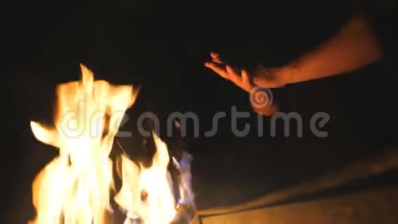 低视角的年轻游客擦着他的手在一个开放的篝火前从曼格尔在晚上人因火而暖臂视频的预览图