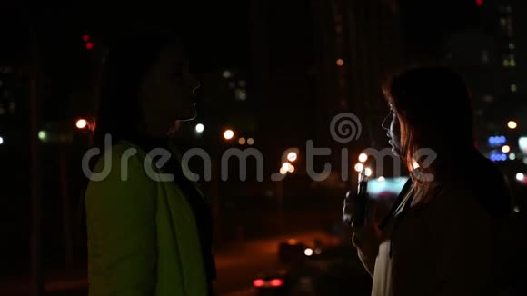两个女朋友在夜城的背景上抽烟女人深夜抽香烟和蒸汽坏习惯视频的预览图