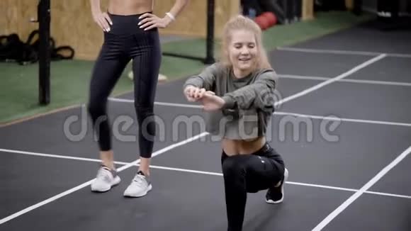 健身房里两个漂亮的年轻女人女孩子在教练面前做伸展运动金发美女看着他们视频的预览图