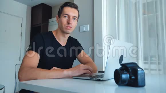 年轻的男性摄影师使用笔记本电脑处理图像并在家里喝咖啡视频的预览图