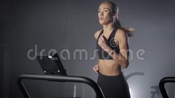在健身房跑步机上滑溜溜的金发女郎一个身材漂亮身材紧绷的女孩在健身房跑步视频的预览图