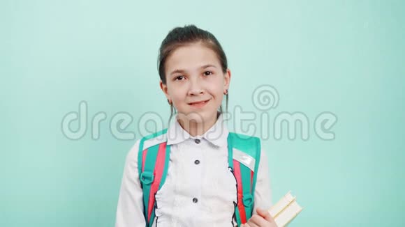 穿着白色衬衫的女学生背着背包手里拿着蓝色背景的书视频的预览图