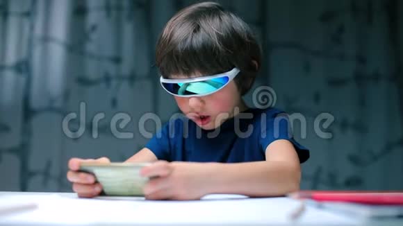 一个男孩戴着眼镜坐在桌子旁使用智能手机视频的预览图