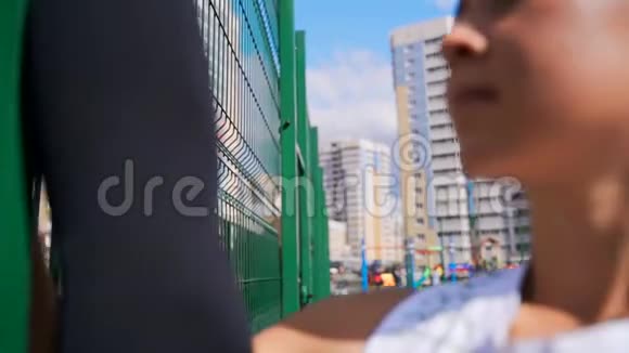 女孩做了一根竖绳站在操场的金属栅栏附近摄像机沿着栅栏移动视频的预览图