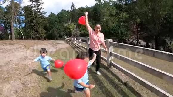亚洲家庭一起在春天的花园里玩着手持心形的红色气球跑步幸福家庭和视频的预览图