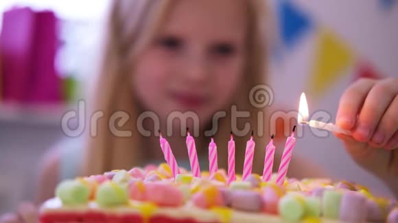金发白种人的小女孩在彩虹蛋糕上点燃蜡烛许下一个愿望并在生日聚会上把它们吹灭重点视频的预览图