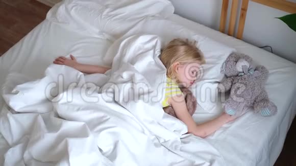 金发的小女孩睡在大床上床上铺着白色的床上用品上景孩子们做梦童年平静夜晚4K录像视频的预览图