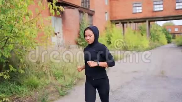 穿着黑色运动服的女孩穿过一家废弃工厂的领地视频的预览图