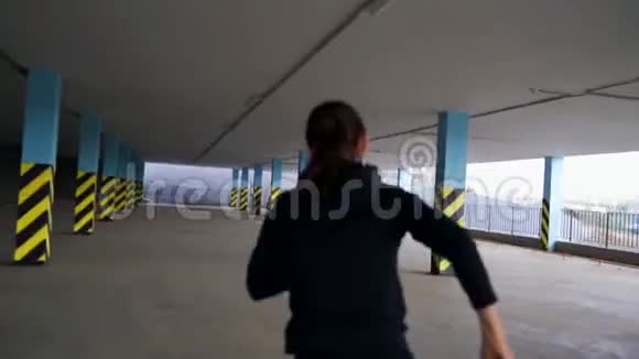 小女孩沿着室内停车场的柱子跑用相机摇动手的视频记录视频的预览图