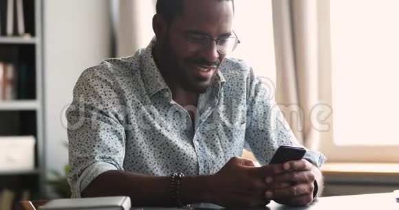 用移动应用程序微笑的非洲年轻人坐在桌子上视频的预览图