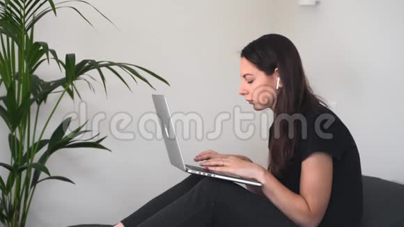 一个姿势不好的年轻女人在家里用笔记本电脑工作在床上用笔记本电脑视频的预览图
