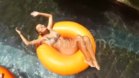 年轻的混合赛女在比基尼放松在游泳池懒河水上公园高清慢速运动视频的预览图