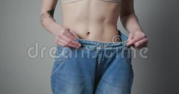 女人展示她的体重减轻和穿她的旧牛仔裤大牛仔裤里的苗条女孩展示了她如何减肥视频的预览图