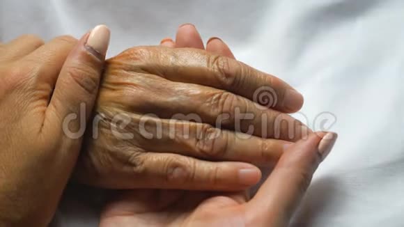 女人握着母亲的手轻轻地抚摸着她的手表现出关怀或爱女儿安慰老人布满皱纹的手臂视频的预览图