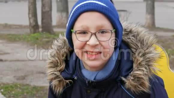 早春十岁的可爱开朗的少年戴着眼镜在操场上荡秋千视频的预览图