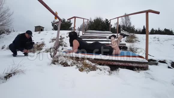 摄影师拍摄穿着黑色夏装的女孩和VR眼镜躺在河边的雪地上的照片对比视频的预览图