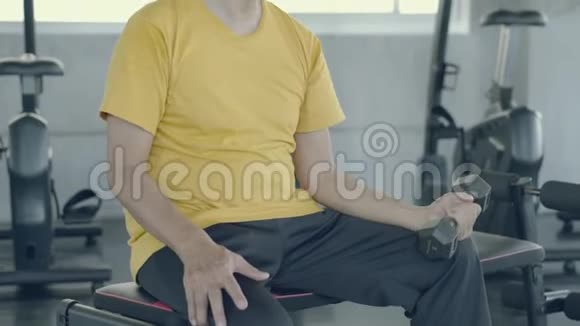 亚洲老人坐着举起哑铃训练手臂加强肌肉在健身房退休视频的预览图