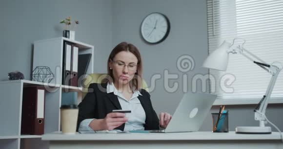商务女性在办公室用笔记本电脑在线购物年轻女子手里拿着银行信用卡用电脑购买视频的预览图