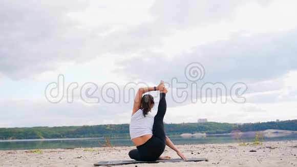 河岸上的一个女孩坐在瑜伽姿势中腿伸了起来视频的预览图