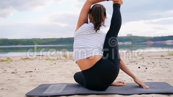 河岸上的一个女孩坐在瑜伽姿势中腿伸了起来视频的预览图