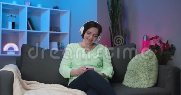 在家听音乐的高中生快乐戴无线耳机的老年妇女视频的预览图