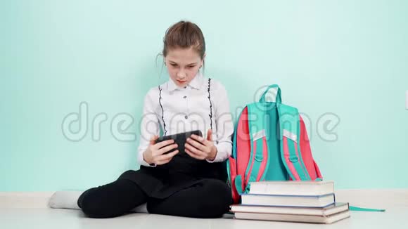 一个穿着白色衬衫的年轻女学生坐在地板上手里拿着一部智能手机旁边是一个背包视频的预览图