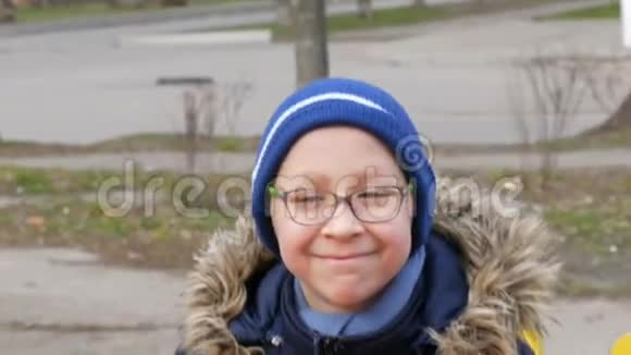 早春十岁的可爱开朗的少年戴着眼镜在操场上荡秋千视频的预览图