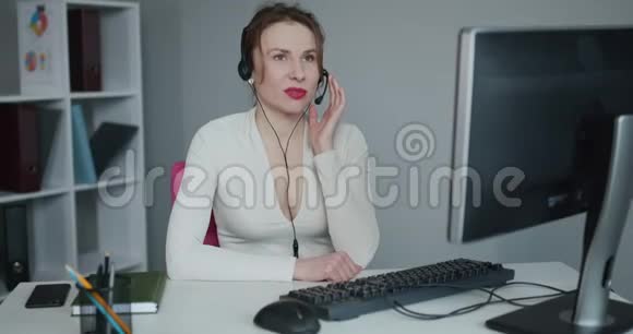 漂亮的女人坐在办公桌前的行政椅上带麦克风的耳机举行视频会议视频的预览图