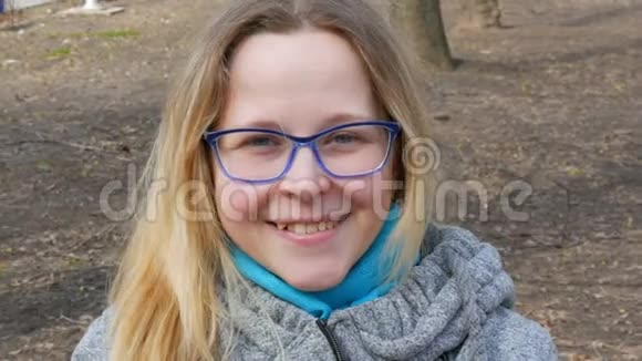 美丽的年轻女子金发碧眼戴着眼镜坐在春天的公园里微笑视频的预览图