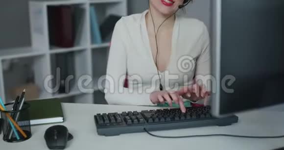 支持手机运营商在耳机使用个人电脑呼叫中心员工在办公室工作时的女士微笑视频的预览图