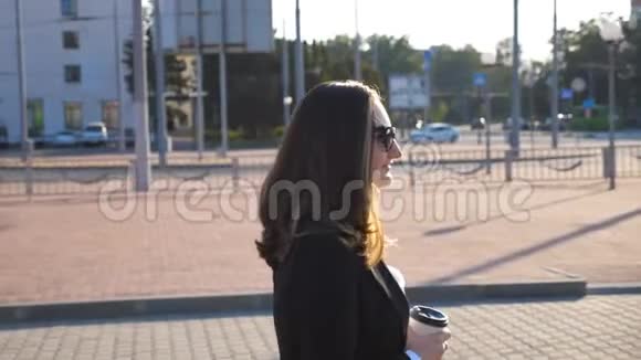 阳光明媚的一天带着一杯咖啡在汽车停车场附近散步的年轻微笑的女商人快乐的商界女性视频的预览图