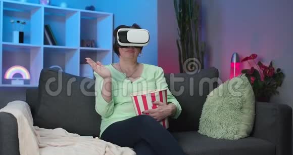 高级女性晚上佩戴VR耳机触摸虚拟屏幕女人坐在沙发上戴着虚拟现实耳机视频的预览图