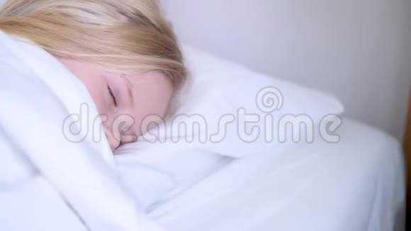 睡着的金发小女孩一大早就躺在大床上铺着白色床上用品孩子们做梦童年平静视频的预览图