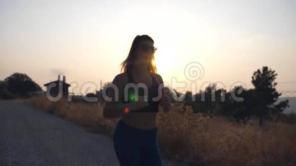在日落时在乡间小路上慢跑的运动女孩年轻女子在户外跑步健康的积极生活方式慢动作关闭视频的预览图