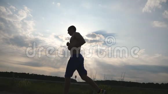 日落时分在乡间小路上慢跑的肌肉男剪影男子慢跑训练马拉松跑户外运动员视频的预览图