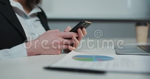 女商人在办公室里拿着笔记本电脑坐在办公桌前一边用智能手机视频的预览图