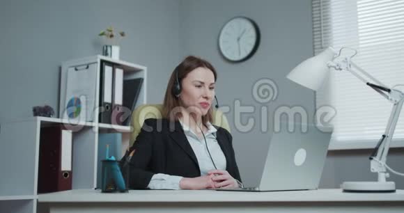 戴着耳机的女人拿着纸质的财务报告在网络摄像头上讲话打着视频电话商务教练看着视频的预览图