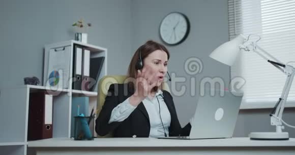 在网络研讨会上戴着耳机的快乐女人用网络摄像头说话看着笔记本电脑女商人用视频说话视频的预览图