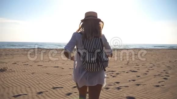 穿比基尼和衬衫的快乐女孩带着背包在海滩上奔向大海美丽的女人在海边慢跑视频的预览图