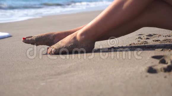美丽的女性腿躺在沙滩上在海边放松年轻女子坐在海岸上晒黑阳光明媚视频的预览图