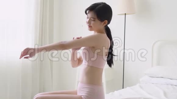 美丽的年轻亚洲女人微笑着在卧室里涂防晒霜乳液视频的预览图