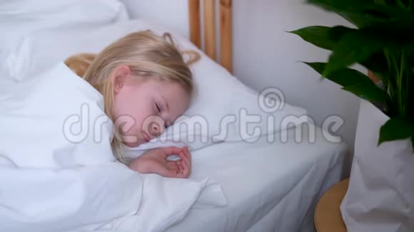 清晨睡在大床上的金发小女孩铺着白色床上用品上景孩子们做梦童年视频的预览图