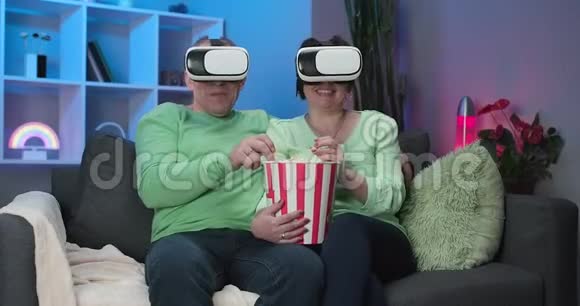 令人兴奋的老夫妻在客厅里玩VR眼镜在家看电影安老夫妇视频的预览图